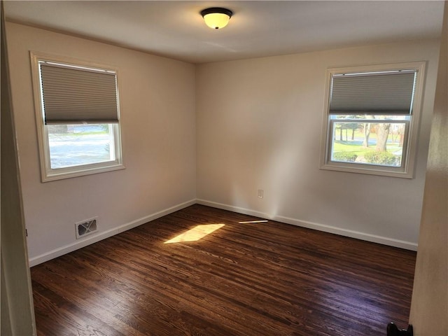 empty room featuring visible vents, baseboards, a healthy amount of sunlight, and dark wood-style floors