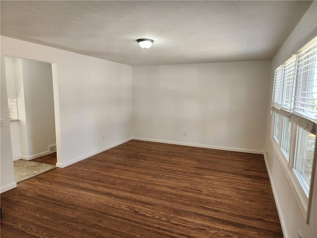 unfurnished room featuring visible vents, baseboards, and dark wood-style floors