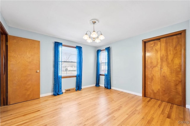 unfurnished bedroom with light wood finished floors, visible vents, baseboards, and an inviting chandelier