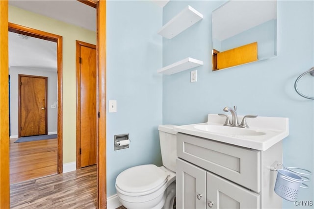 half bathroom with vanity, toilet, wood finished floors, and baseboards