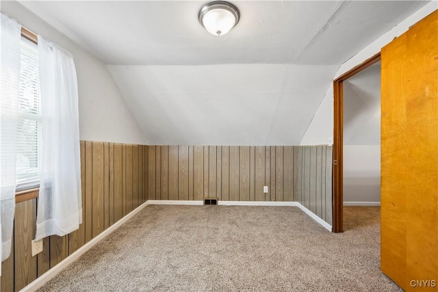 bonus room with wooden walls, carpet flooring, and vaulted ceiling