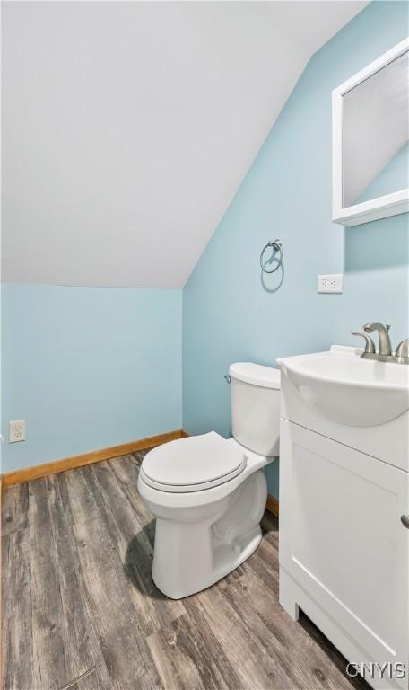 bathroom featuring toilet, wood finished floors, baseboards, vanity, and vaulted ceiling