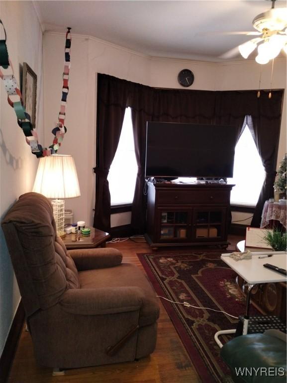 living room featuring wood finished floors, ornamental molding, and a ceiling fan