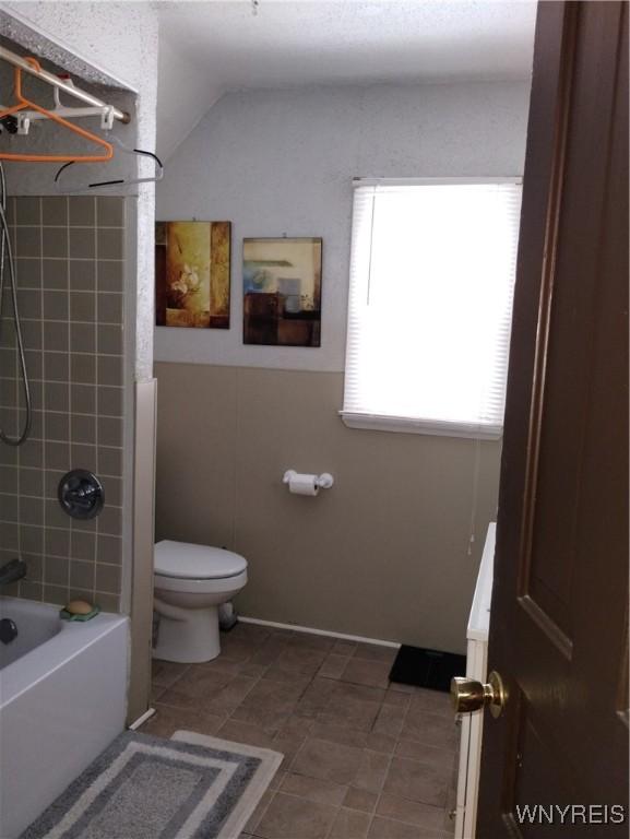 full bath featuring tile patterned flooring, tub / shower combination, toilet, and vaulted ceiling