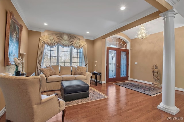 living area with decorative columns, baseboards, wood finished floors, and ornamental molding