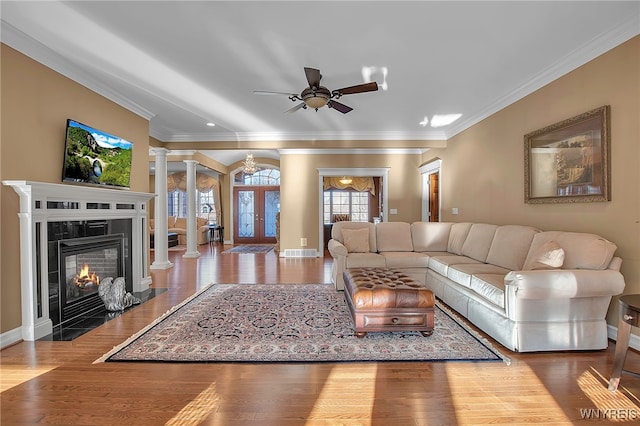 living area with wood finished floors, crown molding, baseboards, and decorative columns