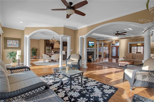 living room with wood finished floors, decorative columns, arched walkways, ornamental molding, and a lit fireplace