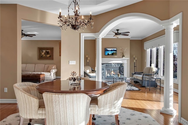 dining room featuring decorative columns, wood finished floors, arched walkways, and a high end fireplace