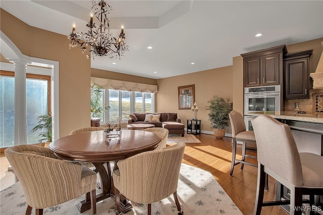 dining space with baseboards, ornate columns, light wood-style flooring, recessed lighting, and a raised ceiling