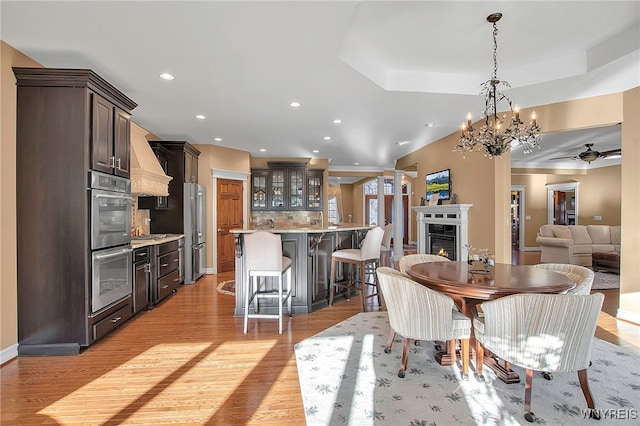 dining space with light wood finished floors, recessed lighting, a raised ceiling, and a lit fireplace