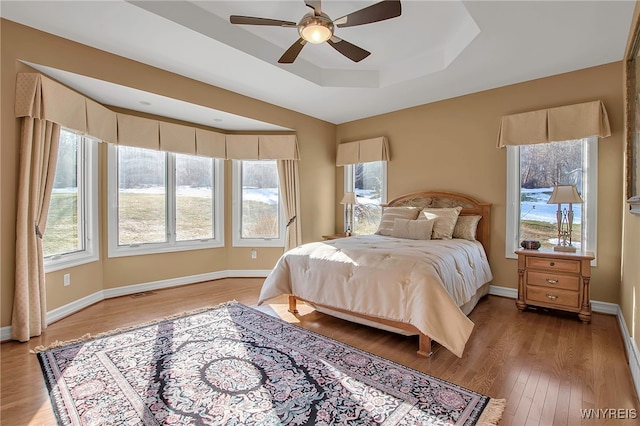 bedroom with visible vents, baseboards, light wood-type flooring, a tray ceiling, and a ceiling fan