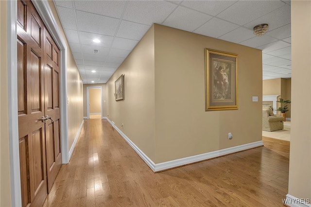 hallway featuring baseboards, a paneled ceiling, and light wood-style floors