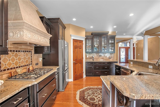 kitchen featuring premium range hood, light wood-style flooring, a sink, stainless steel appliances, and ornate columns