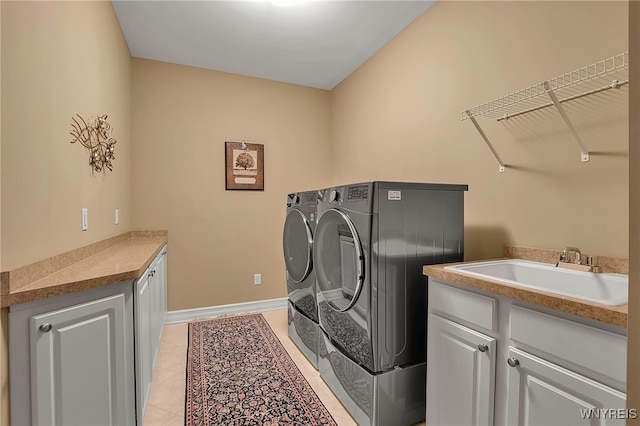 clothes washing area with light tile patterned floors, baseboards, cabinet space, a sink, and independent washer and dryer