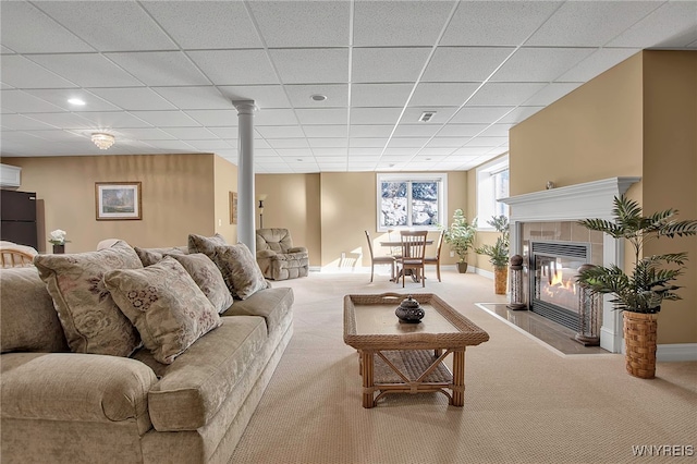 living area with visible vents, baseboards, a drop ceiling, a tiled fireplace, and carpet flooring