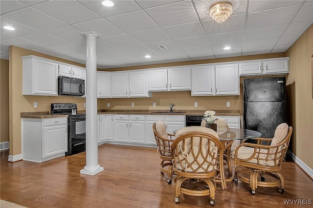 kitchen featuring black appliances, wood finished floors, ornate columns, and a sink