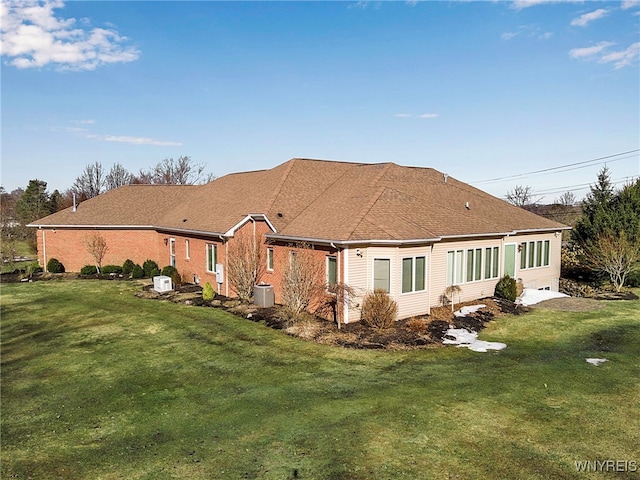 rear view of house featuring a lawn, brick siding, and roof with shingles