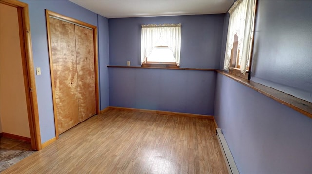 unfurnished bedroom featuring a baseboard heating unit, baseboards, light wood-style floors, and a closet