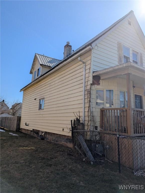 view of side of property with metal roof, a lawn, a chimney, and fence