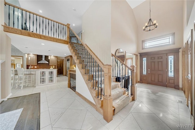 foyer entrance with light tile patterned floors, stairway, a notable chandelier, and a high ceiling