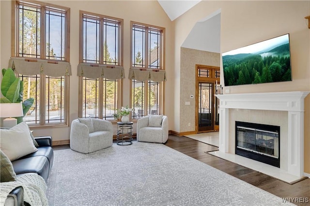 living area featuring a tile fireplace, high vaulted ceiling, baseboards, and wood finished floors