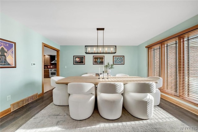 dining space with a notable chandelier, visible vents, baseboards, and wood finished floors