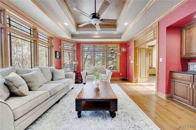 living room with baseboards, ceiling fan, ornamental molding, a raised ceiling, and light wood-type flooring