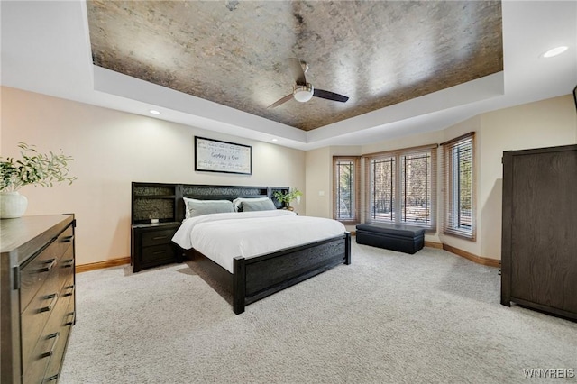 bedroom featuring light colored carpet, a raised ceiling, and baseboards