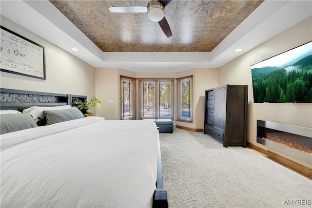 bedroom with a glass covered fireplace, a raised ceiling, baseboards, and light carpet