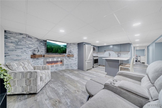 living room featuring a glass covered fireplace, recessed lighting, light wood-style floors, and a drop ceiling