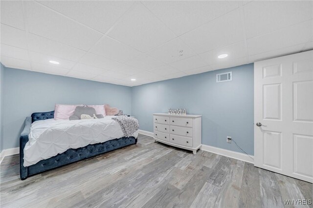 bedroom with a drop ceiling, visible vents, baseboards, and wood finished floors