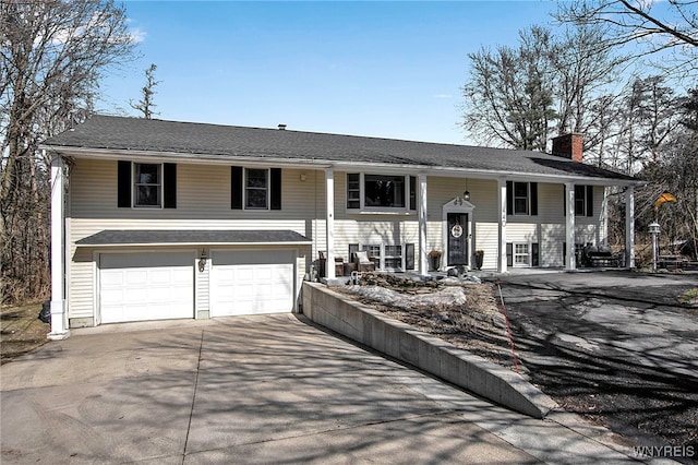 bi-level home with a chimney, an attached garage, and concrete driveway