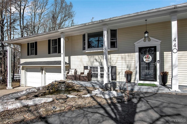 raised ranch featuring a garage, covered porch, and driveway