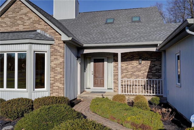 entrance to property with brick siding, a porch, and a shingled roof