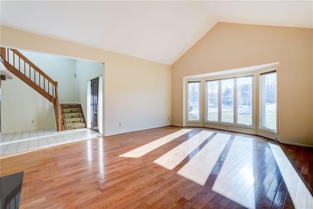 unfurnished living room featuring stairway, high vaulted ceiling, and wood finished floors