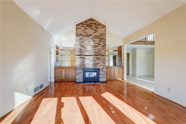 unfurnished living room featuring visible vents, a brick fireplace, high vaulted ceiling, and light wood-type flooring