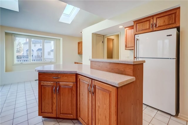 kitchen with light tile patterned floors, brown cabinetry, a skylight, freestanding refrigerator, and light countertops