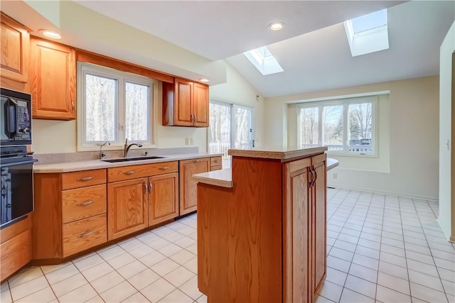 kitchen with black appliances, a sink, a center island, vaulted ceiling with skylight, and light countertops