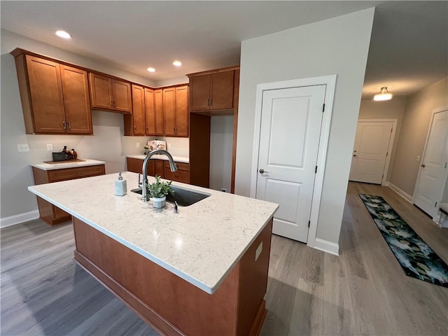 kitchen featuring baseboards, recessed lighting, light wood-style floors, brown cabinetry, and a sink