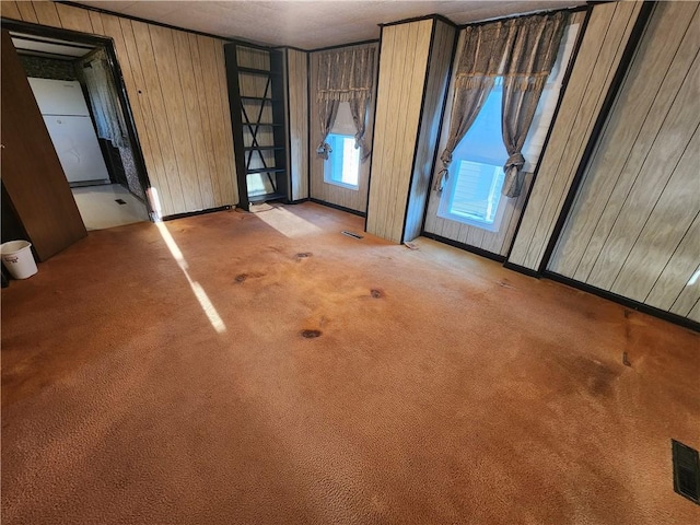 empty room featuring wooden walls, visible vents, and light carpet