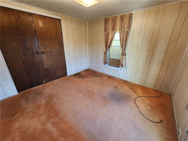 unfurnished bedroom with a closet, visible vents, carpet floors, and wood walls