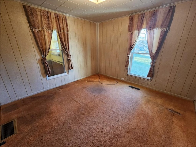 empty room featuring visible vents, carpet floors, and wood walls