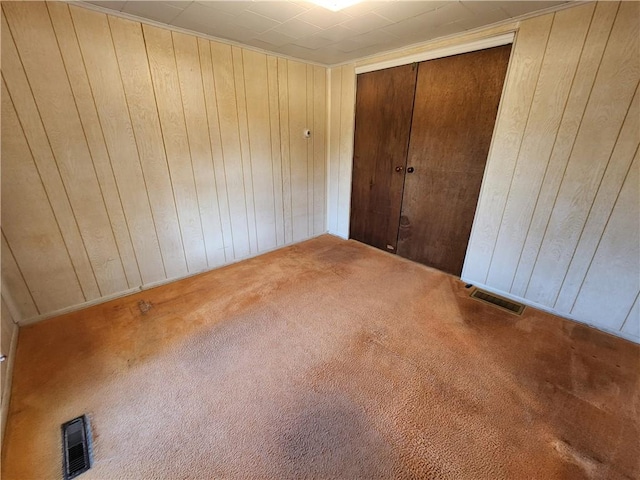 unfurnished bedroom with visible vents, carpet floors, a closet, and wood walls