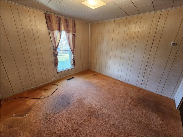 unfurnished room with visible vents, wooden walls, and carpet floors