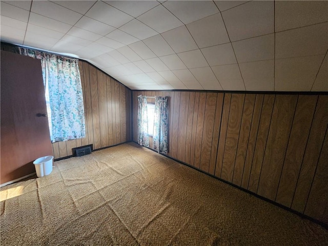 spare room with visible vents, light carpet, wood walls, and vaulted ceiling