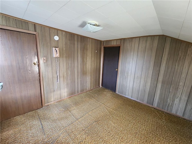 unfurnished room with lofted ceiling, wooden walls, and carpet floors