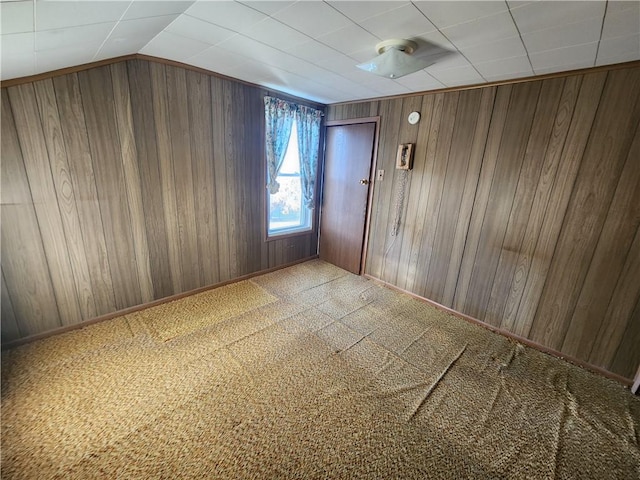 carpeted spare room featuring wood walls, baseboards, and lofted ceiling