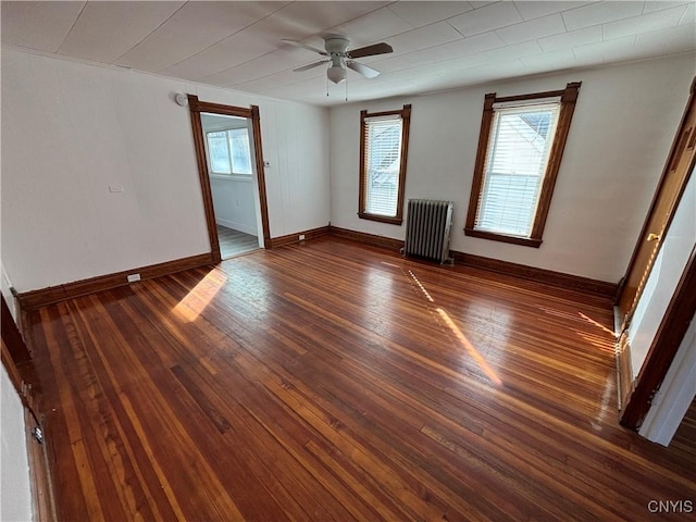 empty room featuring a healthy amount of sunlight, radiator heating unit, baseboards, and hardwood / wood-style flooring