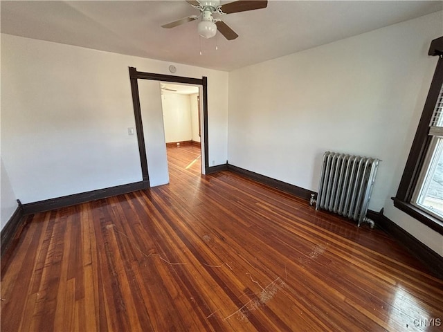 unfurnished room with baseboards, a ceiling fan, dark wood finished floors, and radiator heating unit