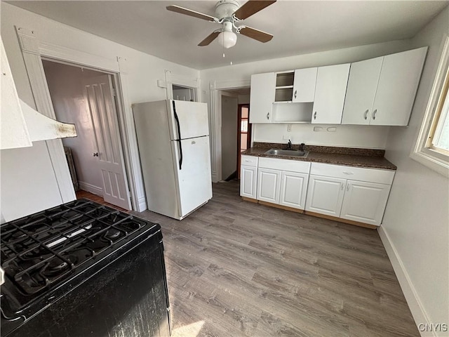 kitchen featuring a sink, open shelves, black gas range, freestanding refrigerator, and white cabinets